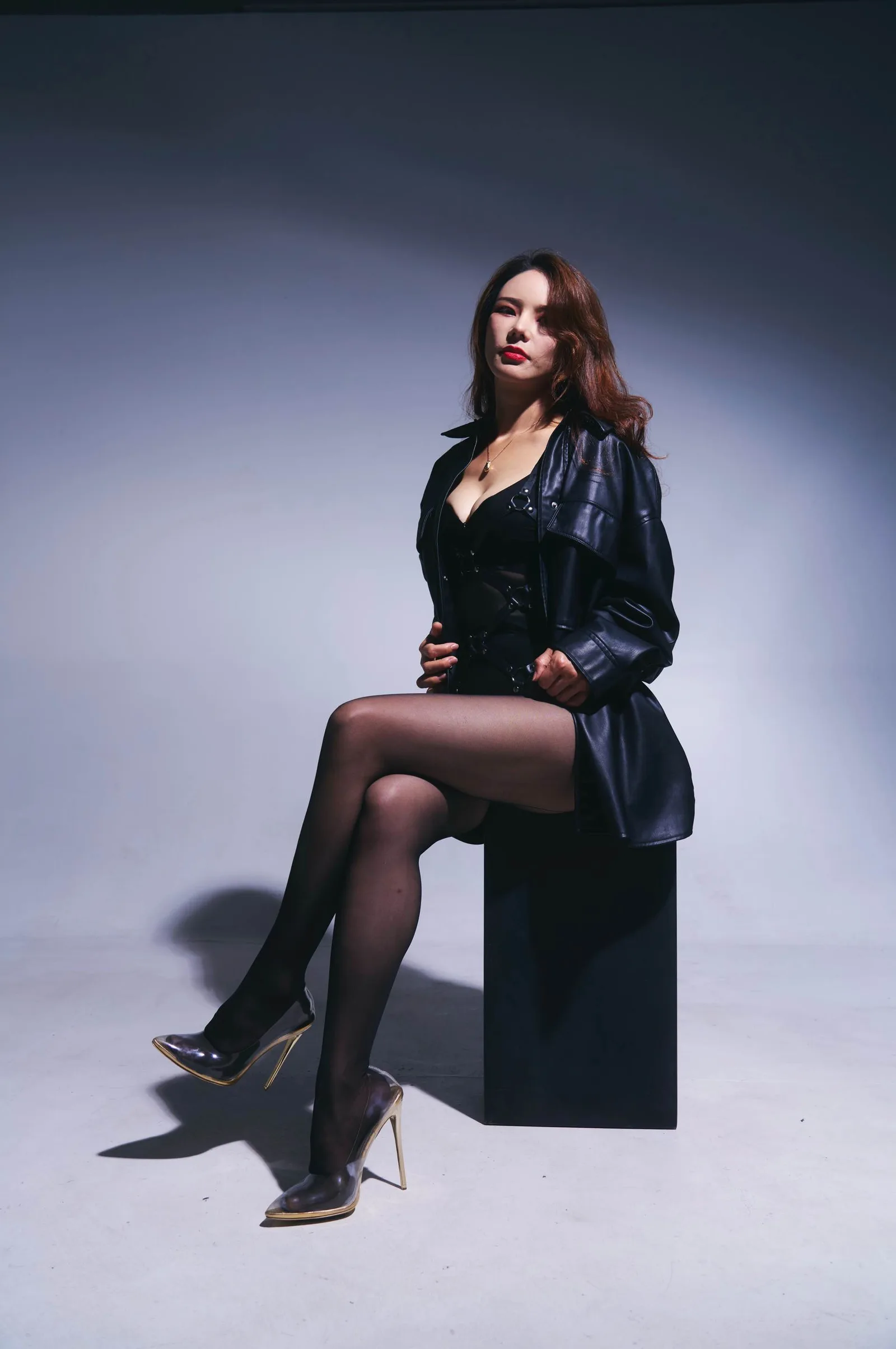 Goddess Sinclair seated in a black leather coat